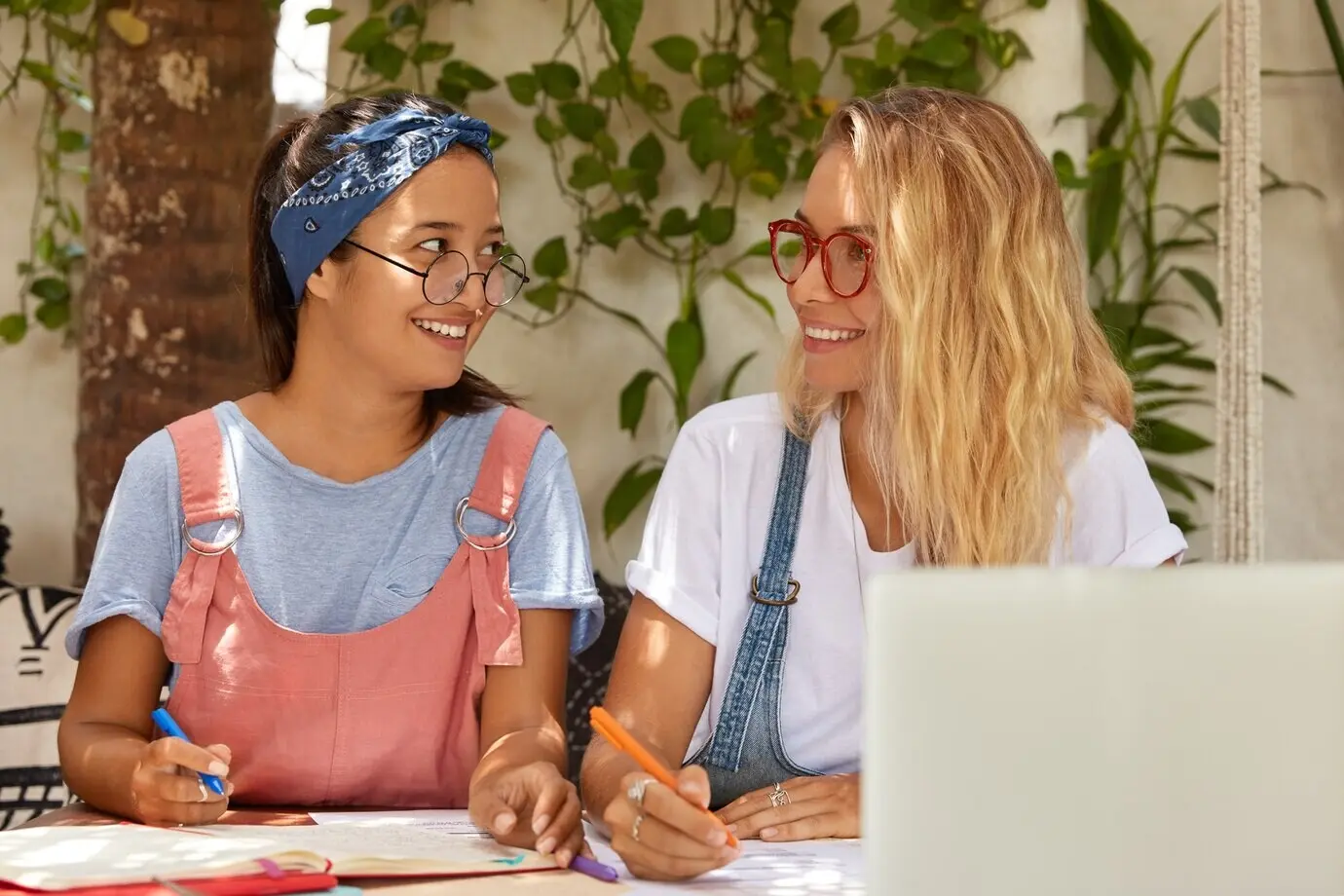 Glückliche, zufriedene, lächelnde jugendliche Person, die am College studiert, hält Stifte und bereitet sich darauf vor, eine Kursarbeit zu schreiben.
